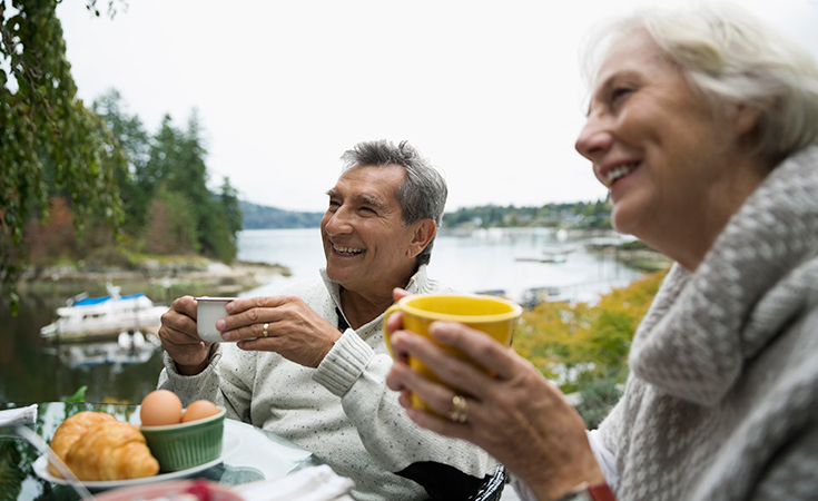 older couple smiling and drinking coffee outside