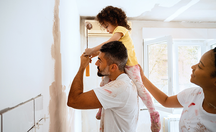 father holding daugther on shoulders while painting a wall
